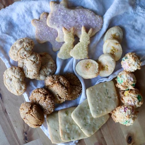 A variety of cookies arranged on a cloth, including decorated shapes, round cookies, and colorful treats.