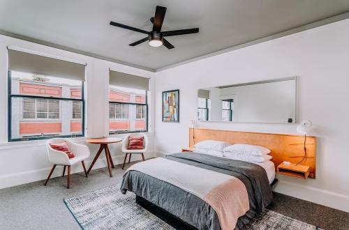 Cozy bedroom with a bed, modern decor, a round table, two chairs, and large windows letting in natural light.