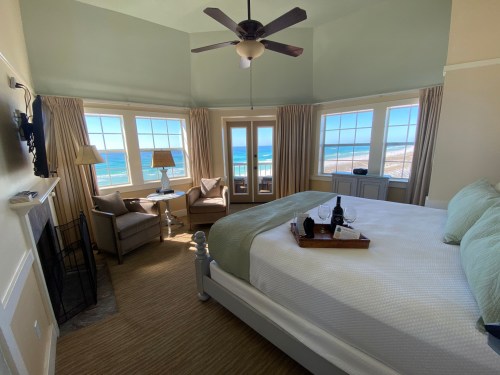 Cozy bedroom with a large window view of the ocean, featuring a king bed, seating area, and soft natural light.