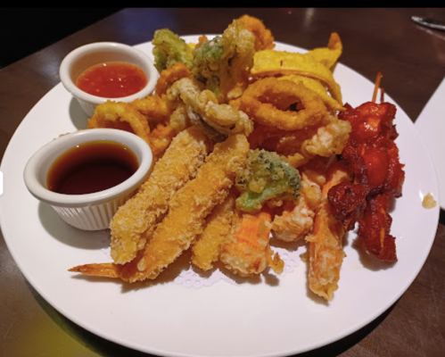 A plate of assorted fried foods, including shrimp, vegetables, and skewers, served with dipping sauces.