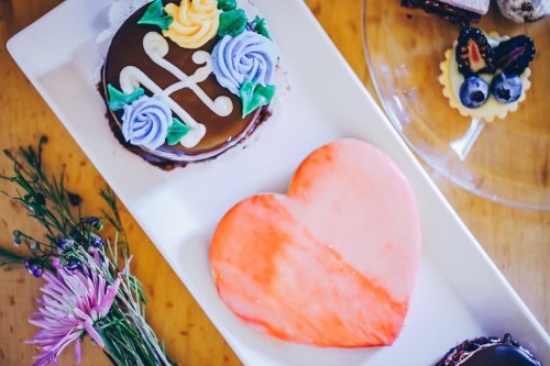 A platter of colorful desserts, including a chocolate cake and a heart-shaped cookie, surrounded by flowers.