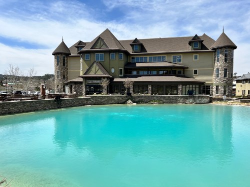 A large, multi-story building with turrets beside a bright turquoise pond under a blue sky.
