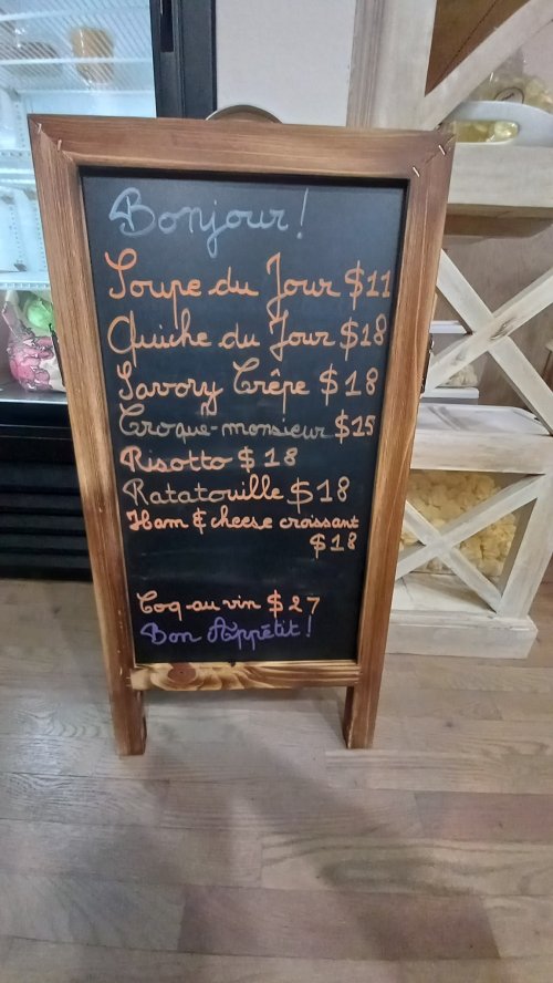 Chalkboard menu displaying daily specials in French, including soup, quiche, crepe, and more with prices listed.