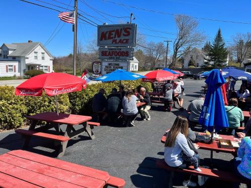 Outdoor dining area at Ken's Place Seafoods, with patrons seated under umbrellas on a sunny day.