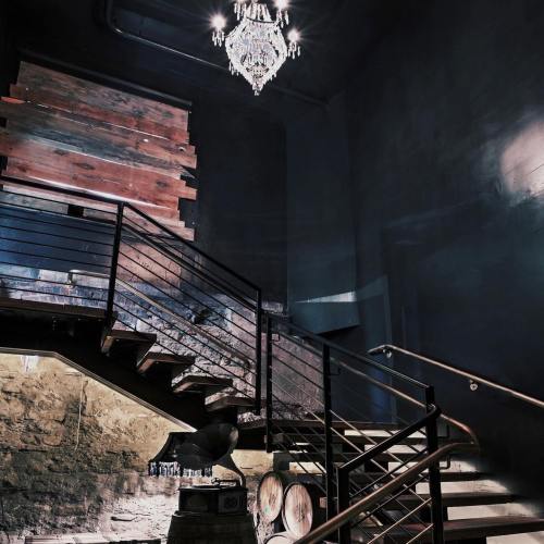 A stylish staircase with a modern chandelier, surrounded by dark walls and wooden accents, leading to a lower level.