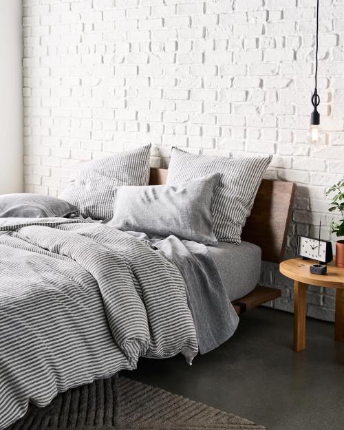 Cozy bedroom with a striped bedding set, wooden headboard, and a small side table with a plant and clock.