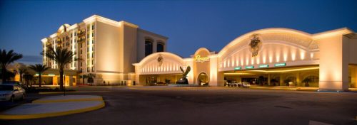 Illuminated entrance of a hotel and casino at dusk, featuring elegant architecture and palm trees.