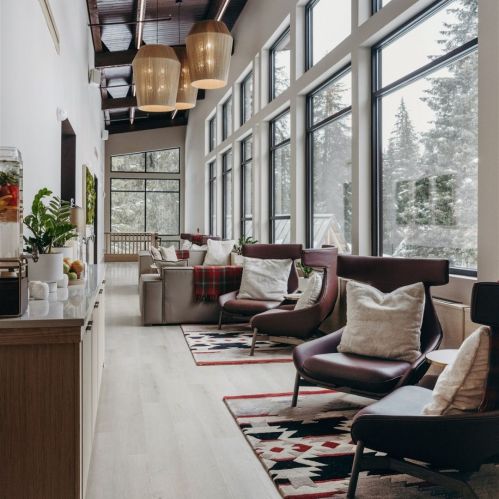 A cozy interior with large windows, modern furniture, and warm lighting, featuring a lounge area and a snack bar.