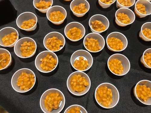 A table covered with small cups filled with baked beans in a glossy orange sauce.