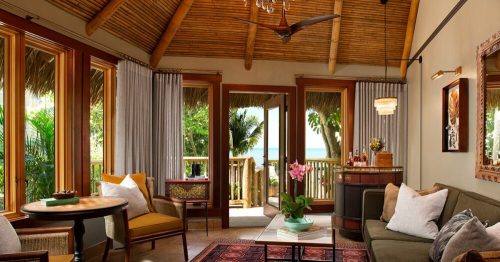 Cozy tropical living room with large windows, a ceiling fan, and a view of the ocean, featuring plants and stylish decor.