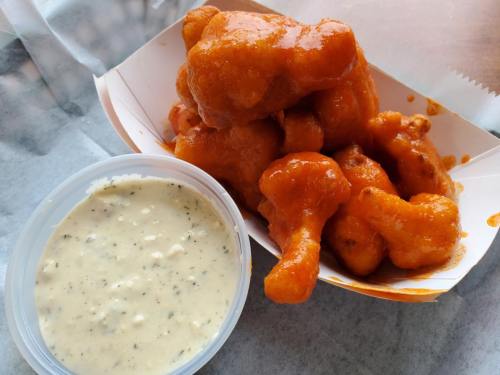 A serving of crispy chicken wings coated in orange sauce, accompanied by a small container of creamy dipping sauce.