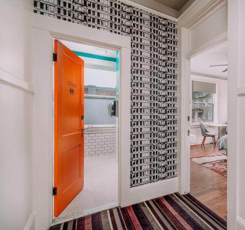 Bright orange door leads to a bathroom, with patterned wallpaper and a view of a modern room beyond.