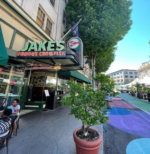 Exterior of Jake's Famous Cornfish restaurant, featuring outdoor seating and colorful pavement in a lively urban setting.