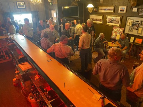 A lively gathering of people socializing in a bar, with a long counter and various decorations on the walls.