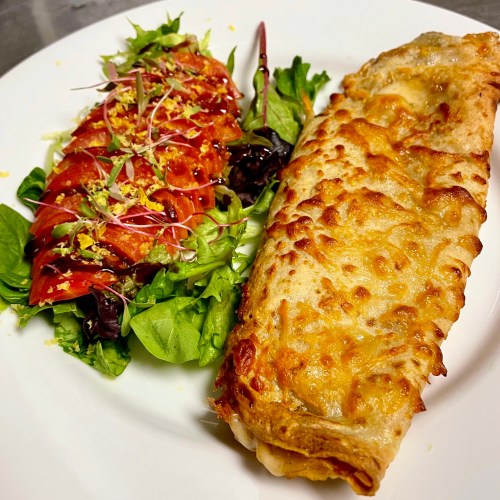 A plate featuring a cheesy baked dish alongside a fresh salad with sliced tomatoes and microgreens.