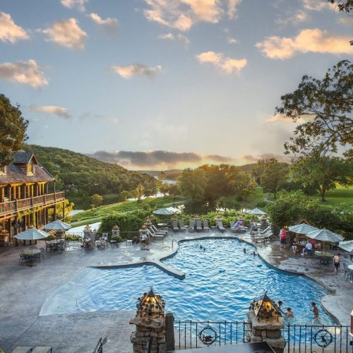 A scenic view of a resort pool surrounded by lush greenery and hills, with guests enjoying the outdoor space.