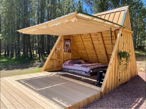 A cozy wooden A-frame cabin with an open front, featuring a bed and surrounded by trees.