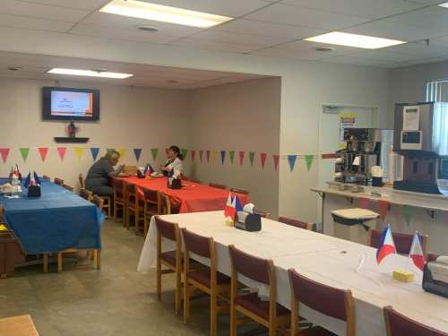 A dining area with colorful tablecloths and flags, featuring two people seated at a table and a coffee station in the background.