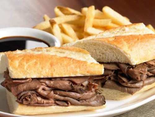 A plate with a roast beef sandwich on a baguette and a side of French fries, accompanied by a dipping sauce.