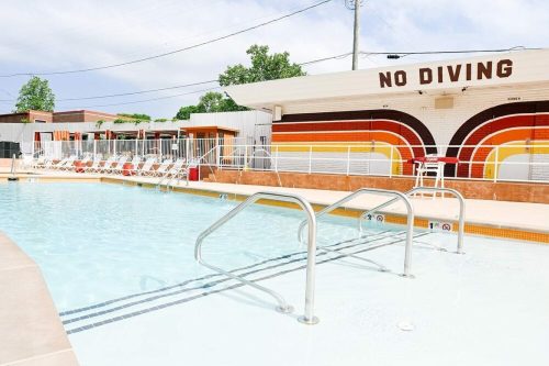 A swimming pool with a "No Diving" sign, surrounded by lounge chairs and a colorful building in the background.
