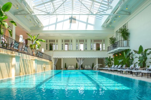 Bright indoor pool with a glass ceiling, surrounded by lush plants and lounge chairs, creating a serene atmosphere.