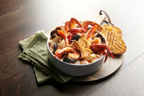 A bowl of assorted seafood, including shrimp, mussels, and clams, served on a wooden board with a green napkin.