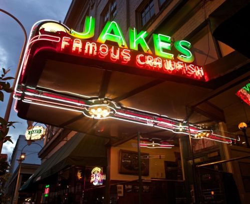 Neon sign for Jake's Famous Crawfish restaurant, glowing in the evening light, with a vintage aesthetic.