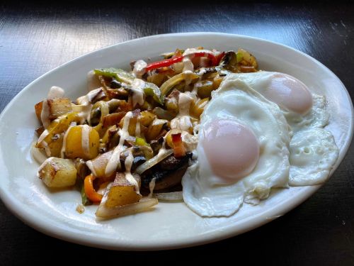 A plate of sautéed potatoes and vegetables topped with two sunny-side-up eggs.