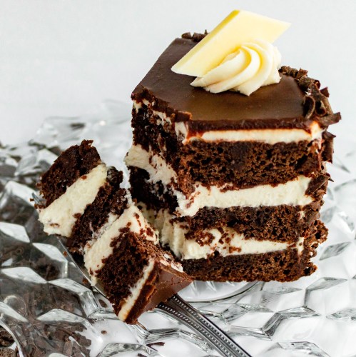 A slice of chocolate cake with layers of cream, topped with a swirl of frosting and a piece of chocolate.