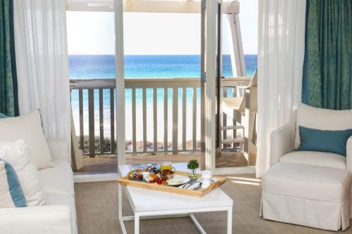 A cozy beachside room with two chairs and a tray of breakfast overlooking the ocean through open doors.