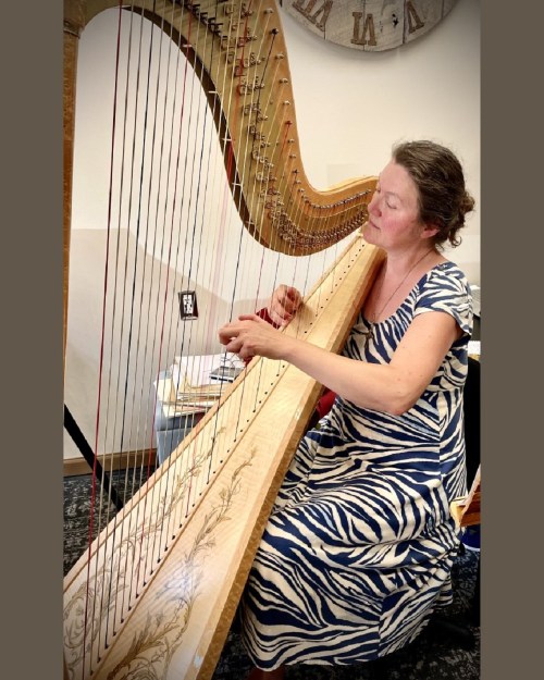 A woman in a zebra-striped dress plays a harp, focused and immersed in her music.