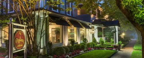 A charming building with a sign, surrounded by lush greenery and colorful flowers, illuminated in the evening light.