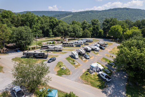 Aerial view of a campground with RVs parked along winding paths, surrounded by trees and mountains in the background.