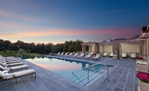 A serene outdoor pool area at sunset, featuring lounge chairs and lush greenery in the background.