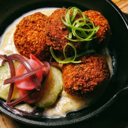 Crispy golden croquettes served on a bed of creamy sauce, garnished with green onions and accompanied by pickled vegetables.