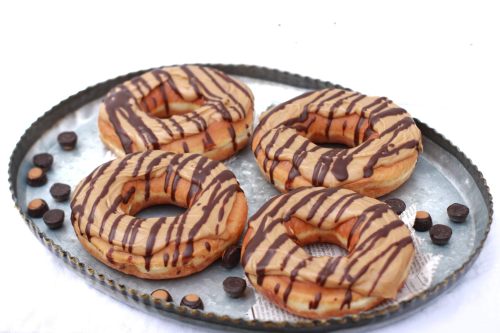 A tray of four donuts drizzled with chocolate and peanut butter, surrounded by chocolate chips.