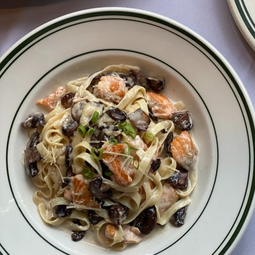 A bowl of fettuccine pasta with salmon, mushrooms, and green onions in a creamy sauce.