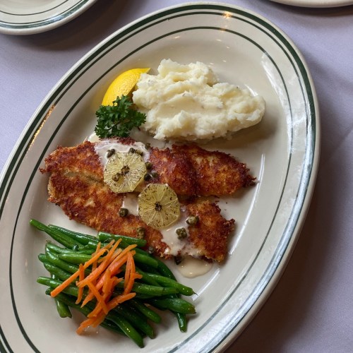 A plate of fried fish with lemon, mashed potatoes, and green beans with carrots, garnished with parsley.