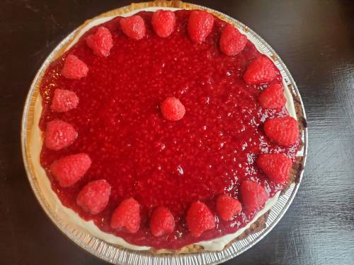 A round raspberry cheesecake topped with a glossy raspberry glaze and fresh raspberries around the edge.