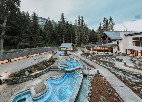 A serene outdoor spa area with winding pools, surrounded by trees and a modern building in the background.