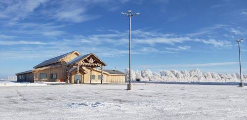 A wooden building in a snowy landscape, with clear blue skies and frosted trees in the background.