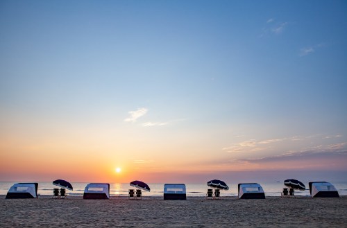 A serene beach at sunrise with cabanas and umbrellas lined up along the shore, reflecting calm waters.