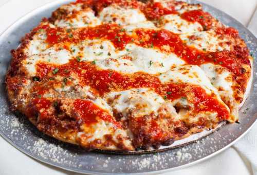 A freshly baked pizza topped with melted cheese, marinara sauce, and herbs on a silver serving tray.