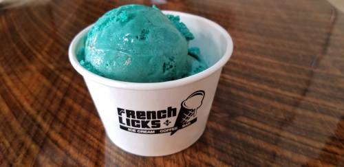 A cup of bright blue ice cream from French Licks, sitting on a wooden surface.