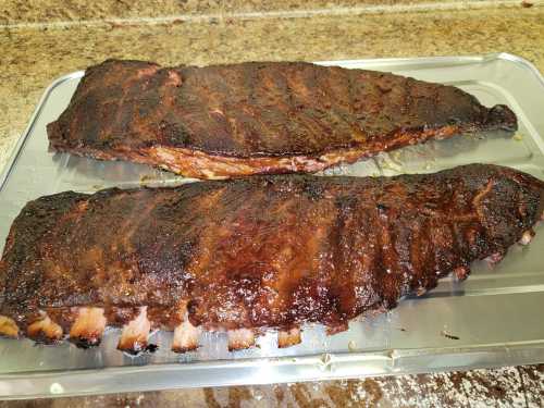 Two large, smoked ribs with a dark, caramelized crust resting on a silver tray.