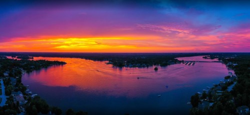 A vibrant sunset over a tranquil lake, with colorful skies reflecting on the water and silhouettes of trees and boats.