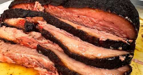 Sliced smoked brisket with a dark, crispy crust and tender pink meat, arranged on a cutting board.