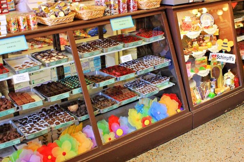 A display case filled with various chocolates and confections, decorated with colorful paper flowers.