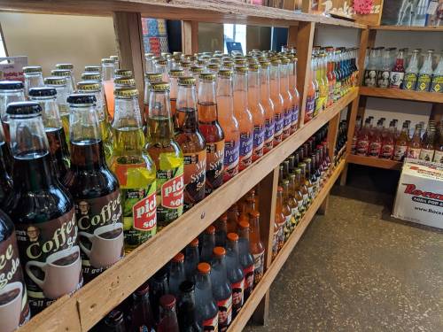 A wooden shelf filled with various colorful soda bottles in a store.