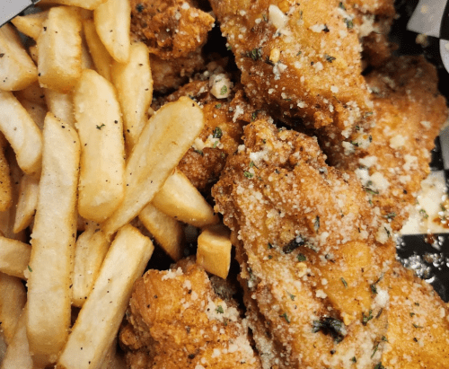 A close-up of crispy fried chicken wings sprinkled with herbs and garlic, served with golden French fries.